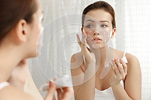 Teen girl with acne problem applying cream near mirror