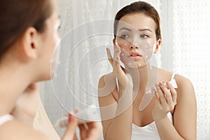 Teen girl with acne problem applying cream near mirror photo