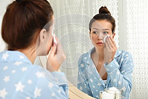 Teen girl with acne problem cleaning face near mirror in bathroom