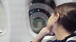 Teen girl aviation aircraft concept. Young girl looks out the airplane sitting by the window. Lifestyle flight at night