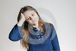 A teen girl in a blue dress with a headache holding her head with her right arm and not looking at a camera