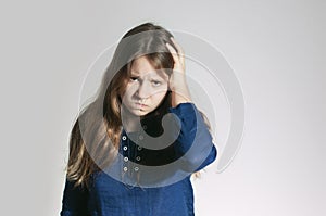 A teen girl in a blue dress with a headache holding her head with one arm looking at camera