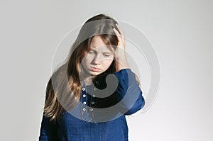 A teen girl in a blue dress with a headache holding her head with one arm not looking at a camera