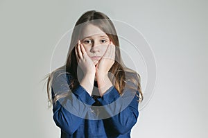 A teen girl in a blue dress with a tooth pain holding her cheeks with both arms over white background