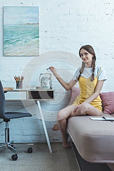 teen girl with braids putting dollar banknote into glass jar