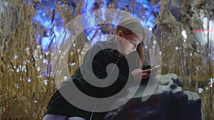 Teen girl browsing internet in smartphone loaning on stone in evening park.