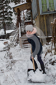 Teen girl cleans snow near a rural house. Winter.