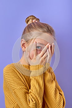 teen girl covers face with hands and looks furtively between fingers, afraid of something