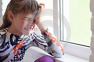 Teen girl crying a lot while sitting by the window in the room, close-up