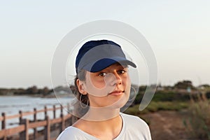 Teen girl in dark blue baseball cap standing by the sea at sunset. Cap mockup