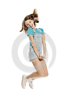 Teen girl in denim overalls in a flying pose, full height. Isolated on a white background.