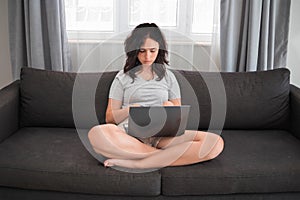 Teen girl doing homework on a laptop. Student girl with laptop on her knees sitting on the couch