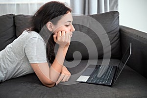 Teen girl doing homework on a laptop. Student girl with laptop laying on the couch