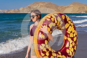 Teen girl with donut lilo against summer landscape of sea and mountains in sunny day. Beautiful young woman in swimwear and