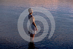 Teen girl in a dress by the sea enters the water