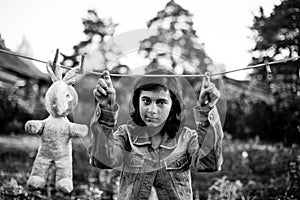 Teen girl dries a toy hare on a clothesline. Black and white photo.