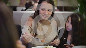 Teen girl eating meat salad in a cafe with friends and listening to music on a smartphone. group of people in a fast