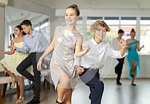 Teen girl in elegant evening dress dances incendiary twist with boy partner during choreography lesson