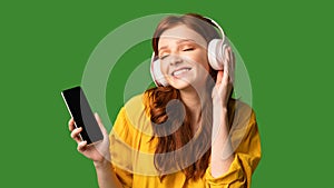 Teen Girl Enjoying Music Holding Smartphone Wearing Headphones, Green Background