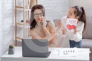 Teen girl giving greeting card to her busy mother, irritated mom not paying attention, taking urgent phone call