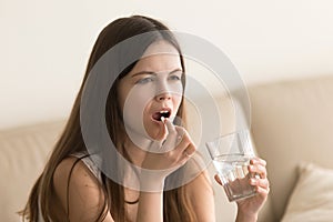 Teen girl with glass of water drinks medicines