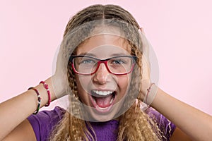 Teen girl with glasses, with long hair scratches her head and is emotional puzzled. Pink studio background.