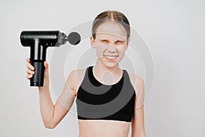 Teen girl grimaces and holds a massage gun. medical-sports device