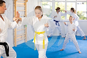 Teen girl at group training in gym practice karate punch block technique with trainer