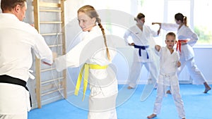 Teen girl at group training in gym practice karate punch block technique with trainer