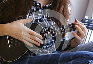 Teen girl hands with ukulele guitar in checked shirt and jeans