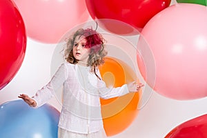 Teen girl in a hat and white dress on a background of big colored rubber air balls