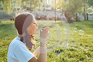 Teen girl having fun in the park - blowing soap bubbles, golden hour