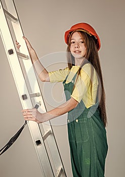 teen girl in helmet and boilersuit on stepladder. child on ladder wear hard hat. kid builder on construction site