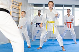 Teen girl with her family in kimonos and colored belts practicing karate with punches during group martial arts class in