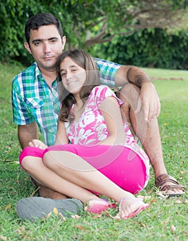 Teen girl and her father sitting in the grass at a beautiful par