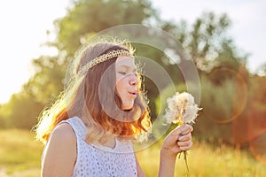 Teen girl with hippie hairstyle blowing on dry dandelions.