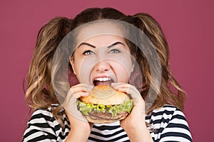 Teen girl holding the beef burger sandwich with happy face and hungry open mouth on isolated pink background