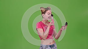 Teen girl holding a brush in her hand and powdering her face. Green screen. Slow motion