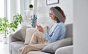 Teen girl holding cell phone using smartphone sitting on sofa at home.