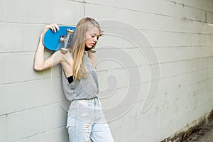 Teen girl holding her skateboard against a wall.