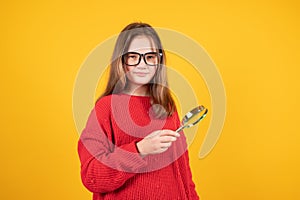 Teen girl holding magnifying glass and looking at something. Young schoolgirl in red sweater and eyeglasses