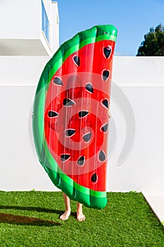 Teen girl holding a watermelon shaped inflatable matress near the swimming pool