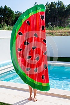 Teen girl holding a watermelon slice shaped inflatable matress near the swimming pool