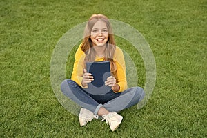 teen girl inspired with new book. relax on green grass. spring leisure time. happy childhood. kid read book outdoor in