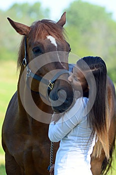 A teen girl kisses her horse in a beautiful field.
