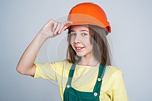 teen girl laborer in protective helmet and uniform on grey background, welcome