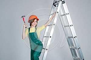 teen girl laborer in protective helmet and uniform on ladder with hammer, constraction