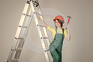 teen girl laborer in protective helmet and uniform on ladder with hammer, constraction