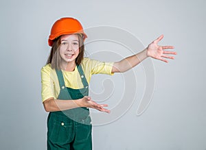teen girl laborer in protective helmet and uniform showing copy space, gesturing