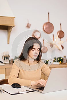 Teen girl with laptop doing homework in bright kitchen with christmas decoration. education and business concept. remote work and